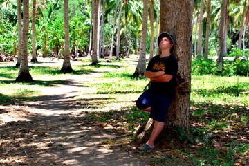 A boy stands by a tree in a tropical forest and looks up, dreaming
