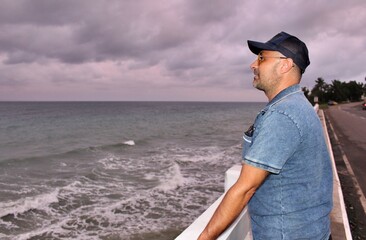 A man standing on a bridge against the backdrop of a stormy sea and gray sky and looking into the distance