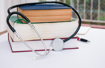 Stethoscope on pile of books isolated on white desk in doctor office. Books and medicine