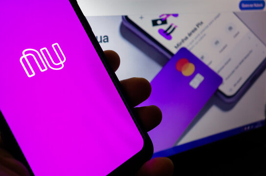Nubank (brazilian fintech) logo visible on smartphone screen, and website homepage on background
