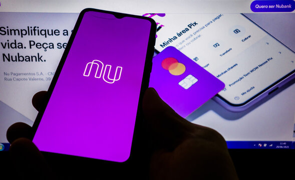 Nubank (brazilian fintech) logo visible on smartphone screen, and website homepage on background