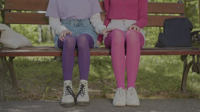 Bright tights on the legs of teenage girls sitting on a park bench. Details in the style of clothing.