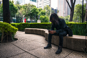 Young man dressed in black watching his cell phone sitting on a bench