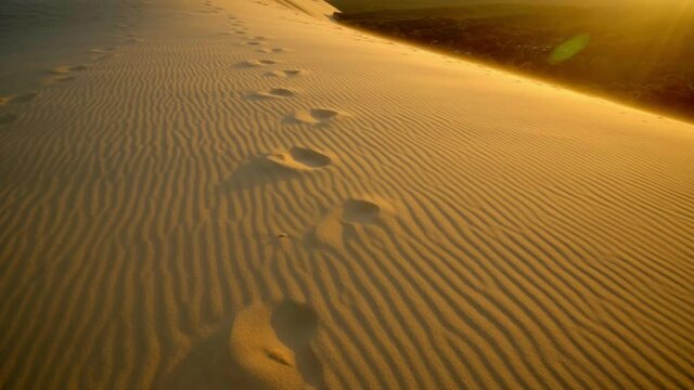 Desertscape of Dune of Pilat at sunset. A row of footprints on golden desert