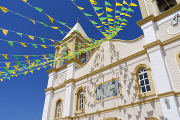 San Jose del Cabo church in Baja California, Mexico. The building is decorated with strings of green and yellow triangular flags against a blue sky.