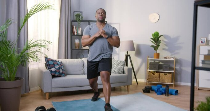 Full length view of the strong active multiracial man doing lunges while training at his cozy apartments with pleased emotions. Stock video