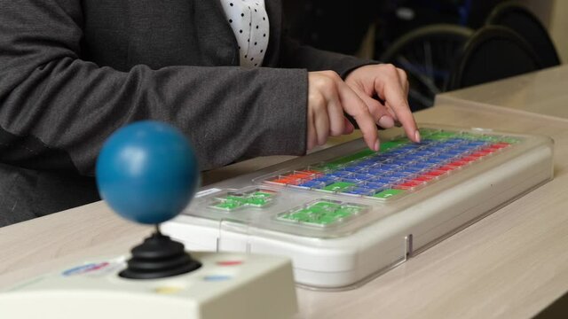An unrecognizable woman with cerebral palsy is typing on the keyboard. A girl with disabilities works on a specially equipped computer