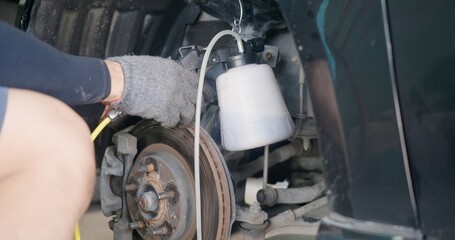 Auto mechanic replacing brake fluid on a vehicle, technician bleed air out of disc brake system in garage workshop, Car repair in a car service - obrazy, fototapety, plakaty