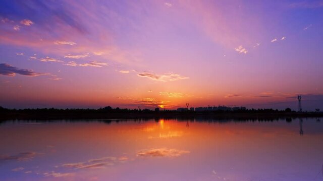 Time-lapse of lake at sunset, clouds in purple sky with reflection on water