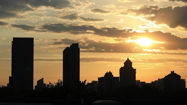 Time-lapse, sunbeam at sunset and silhouettes of city buildings