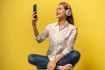 Young women using phone for listening to music via wireless headphone on yellow colour background