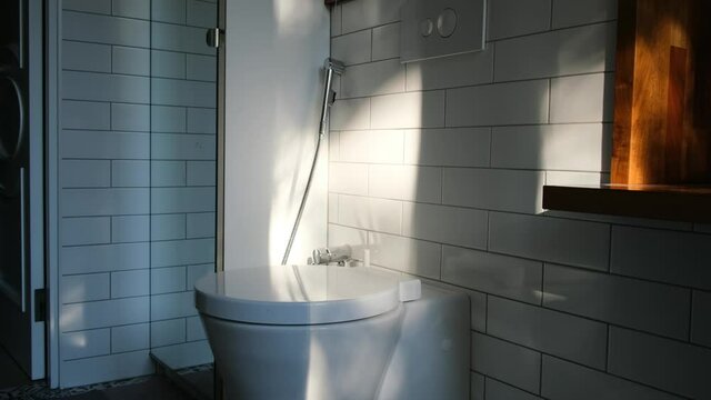 Large shower cabin and white toilet surrounded by white tile wall under bright summer morning sunlight in bathroom at home