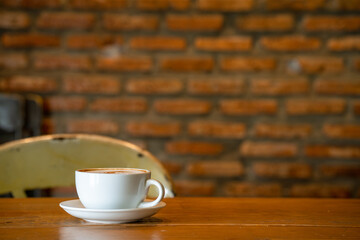 Cup cappuccino on wooden table against bricks wall indoor.