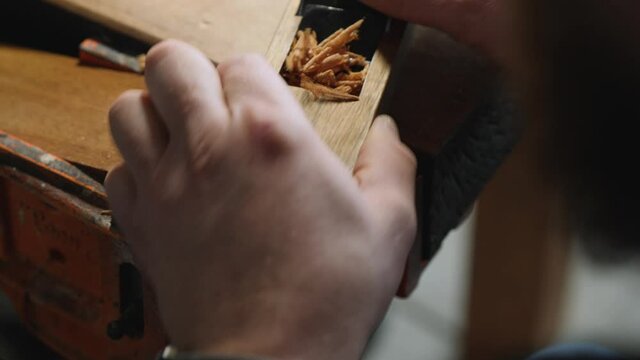 a joiner removes excess thickness from a wooden board using a small plane. work with hand carpentry tools. handmade wood beard comb