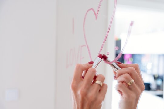 Young blonde woman draws the inscription love and heart with lipstick on the mirror.