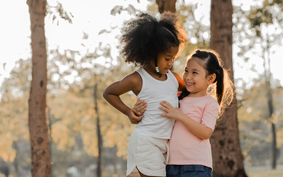Mixed race diverse black African and white Caucasian little girls playing together, happily smiling, hugging with warmth and love in garden or backyard in evening with sunset. Diversity Concept.