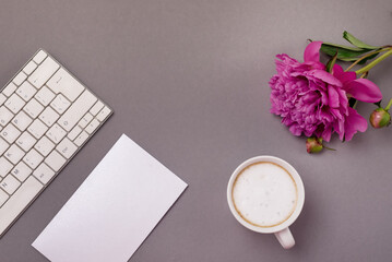 Obraz na płótnie Canvas Workplace with Keyboard Peonies Cup of Coffee and White Blank on Gray Background Top View Flat Lay