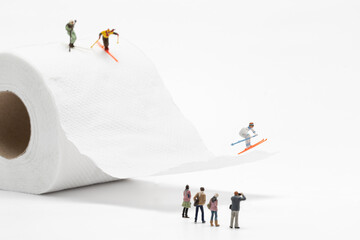 Miniature people skiing on toilet paper on white background.