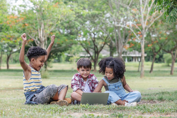 Fototapeta premium Groups of ethnic children sitting on the lawn and having fun using computers together.African American curly hair,positive emotion