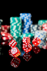 Stack of Casino gambling chips and red dices isolated on reflective black background