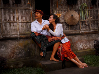 Happy multicultural couple. Romantic concept. Couple in love. Bamboo house. Caucasian wife and Balinese husband wearing traditional clothes. Penglipuran, Bali