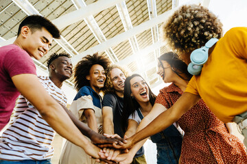 Multiracial happy friends with hands in stack. Multi-ethnic diverse group of college students joining their hands. Stacking hand concept, community, unity and teamwork concept - obrazy, fototapety, plakaty