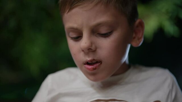 one little boy eating greedily dessert with spoon with chocolate on his lips