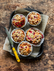 Red currant muffins with crumble in a baking tray on a wooden background, top view