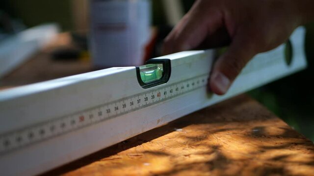 Man's hand holding construction spirit bubble level tool with ruler measuring the horizontal surface of plywood, close up

