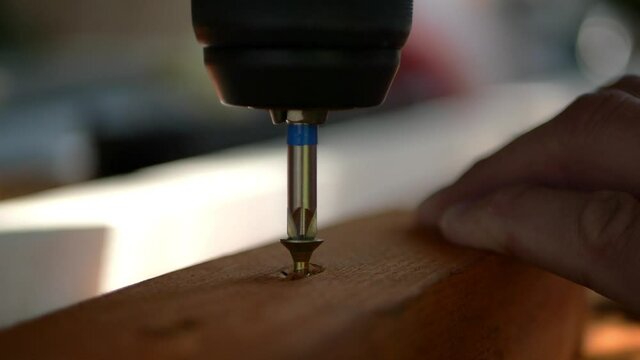 Assembling wood construction while screw is being tightened with cordless screwdriver into batten timber, close up