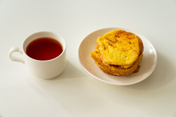 a cup of tea and croutons of bread and egg in a plate on a white table.
