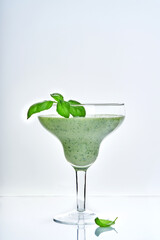 Green vegetable juice or smoothie garnished with leaf of fresh basil in coctail margarita glass isolated on white.