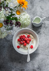 Vegetable milk oatmeal vegetarian porridge with fresh raspberries and a bouquet of summer flowers on a gray concrete background, top view