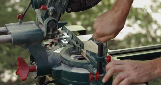 Carpenter fixing wood plank and making slow cross cut on wood plank using miter saw, close-up