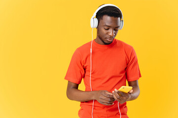 man in orange t-shirt with headphones listening to music yellow background