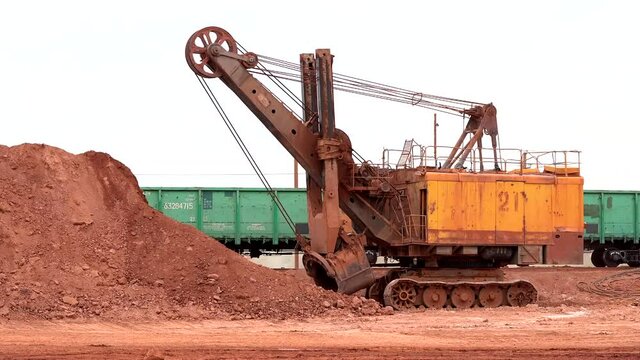 large excavator loads rock with iron or bauxite into the wagons of the quarry against the background of the sky