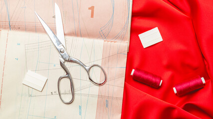 Sewing accessories. Clothes designer work desk. Pattern, scissors, thread,red textile, fabric on...