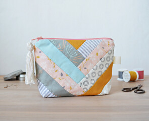 Patchwork zipper pouch with tassel zipper pool, thread spools, little scissors and pins in metal jar on wooden desk over white