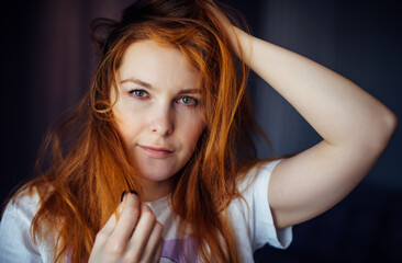 Young sexy red-haired girl touches her tousled hair and looks at camera, close-up. Beautiful well-groomed skin and hair. Image for advertising beauty industry and cosmetology.