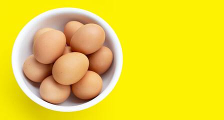 Fresh eggs in white bowl on yellow background. Copy space
