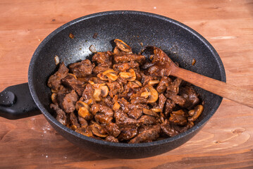 Cooking beef stroganoff with mushrooms - fried cuts of beef with mushrooms in a pan, close-up
