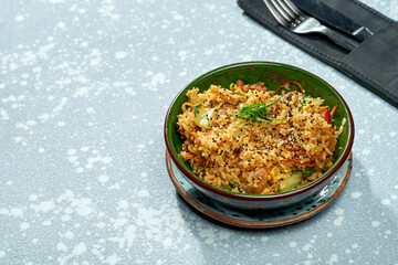 Delicious pan-asian dish - wok rice with chicken, vegetables and sweet and sour sauce in a green bowl on a gray background. Close up, selective focus