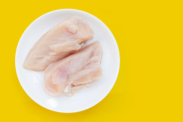 Uncooked raw chicken  breast fillets in white plate on yellow background.