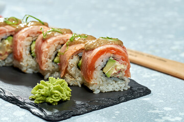 Philadelphia sushi roll with smoked salmon, avocado, cream cheese and sweet sauce on a black plate on a light background