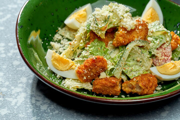 Appetizing salad with chicken breaded and deep fried, parmesan, egg, lettuce and white sauce in a green plate on a blue background