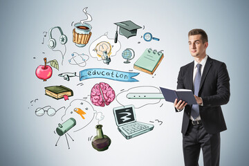 Obraz premium Businessman in suit is holding a book, range of educational icons are drawn behind on light blue wall. Concept of new ideas for start up and postgraduate level of education, mba.