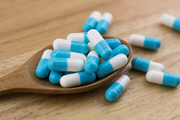 Blue and white capsules pills in a wooden spoon on wooden background, Antimicrobial capsule pills, Antibiotics drug resistance, Pharmaceutical industry.