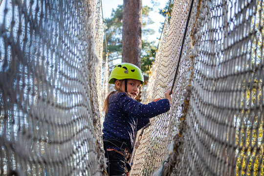 a girl in a green helmet runs the distance in the forest extreme rope park passing through the protective net