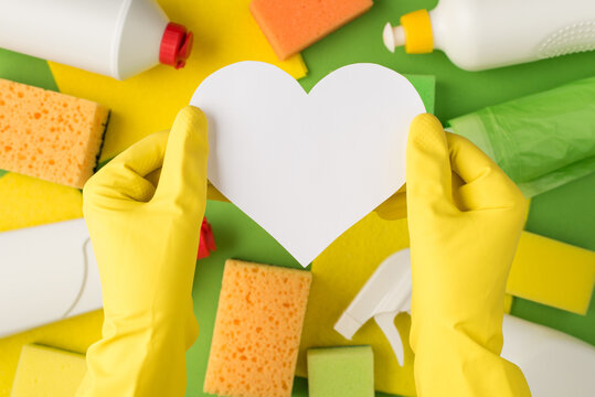Overhead photo of hands in yellow gloves with empty card as heart isolated on the background of equipment for cleaning