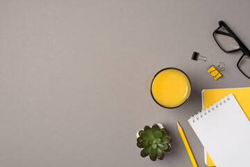 Top view photo of glass of orange juice plant glasses binder clips yellow pencil and reminders on isolated grey background with copyspace
